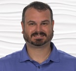 A bearded man in a blue polo shirt smiles against a wavy, white background.