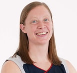 A woman with straight brown hair smiles at the camera, wearing a medbridge athletic jersey.