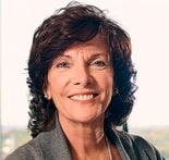 Smiling woman with short, wavy brown hair in a gray sweater, blurred background, illustrating medbridge healthcare.