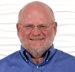 A smiling man with glasses and a beard in a blue shirt is set against a white textured background for medbridge.