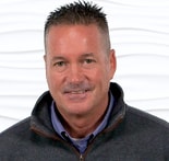 A confident man in a dark jacket and collared shirt smiles, representing his digital healthcare expertise for medbridge.