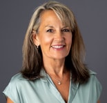 A smiling middle-aged woman in a light green blouse against a gray background, representing digital healthcare at medbridge.