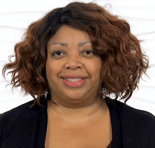 A woman with curly hair smiles slightly in a dark top against a white textured background.