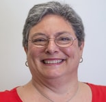 A person with short gray hair and glasses, in a red shirt, smiles enthusiastically about hybrid care combining traditional and digital healthcare solutions for medbridge.