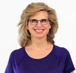 A woman with blonde hair, blue glasses, and a purple top smiles at the camera, representing digital healthcare innovation at medbridge.