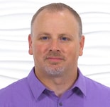 A man in a purple shirt stands confidently against a white background, embodying innovation in digital healthcare for medbridge.
