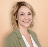Smiling woman in a green blazer, representing medbridge healthcare training, stands before a beige background.