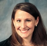 Smiling woman with long brown hair in a black blazer, posing against a neutral background for medbridge digital healthcare.