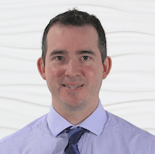 A smiling person in a blue shirt and dark tie against a white textured background, representing medbridge branding.