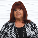 A red-haired woman in a black top and patterned jacket poses confidently against a white background.