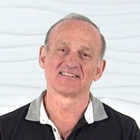A smiling man in a black and gray shirt stands against a wavy white background, symbolizing digital healthcare solutions by medbridge.