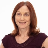 A person with red hair smiles warmly, embodying patient care software against a plain white background for medbridge.
