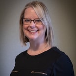 Blonde woman with glasses smiling against a gray background in medbridge.