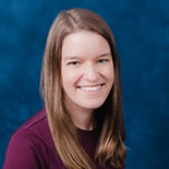 A woman with straight light brown hair in a maroon top smiles at the camera against a blue background, representing medbridge healthcare education.