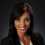 Woman with long dark hair in a black blazer and white top, smiling at the camera, representing excellence at medbridge.
