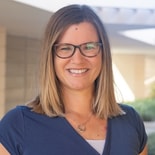 Smiling woman in glasses and a blue top stands outdoors with a blurred building, representing the future of digital healthcare at medbridge.
