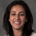 A woman with long dark hair smiles at the camera, wearing a light top and pearl earrings, showing medbridge professionalism.