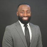 A bearded man in a gray suit smiles confidently against a dark background, representing modern medbridge digital healthcare.