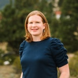 A woman with shoulder-length red hair in a navy top stands outside among trees, symbolizing medbridge's hybrid care future.