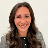 A woman with long brown hair in a gray blazer smiles at the camera, representing medbridge healthcare education.