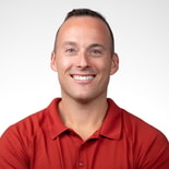 Smiling man with short hair in a red polo shirt, standing against a white background.