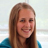 A woman with long straight hair wearing a teal shirt smiles at the camera in a setting typical of digital healthcare or medbridge training.