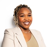 A woman with braided hair smiles confidently at the camera in business attire, representing medbridge.