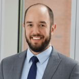 A bearded man in a gray suit smiles indoors, representing Medbridge healthcare education.