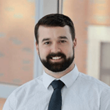 A man with dark hair and a beard stands indoors, dressed professionally, with medbridge branding context.