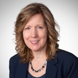A smiling woman with curly hair and a navy blazer represents digital healthcare innovation for medbridge.