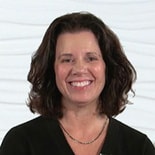 Person smiling with shoulder-length dark hair and a black top, in front of a textured white background for medbridge.