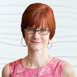 A person with short red hair and glasses, wearing a pink patterned top and hoop earrings, symbolizes Medbridge’s innovative spirit in digital healthcare and education.