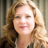 A person with long, wavy blonde hair in professional attire is shown against a neutral background.