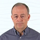 A person with short gray hair in a checkered shirt stands thoughtfully, embodying medbridge's healthcare training ethos.