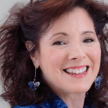 Person with curly brown hair in a blue top and heart-shaped earrings smiling warmly at the camera, symbolizing medbridge's blend of technology and compassion.