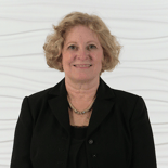 A smiling person with curly hair in a black blazer stands against a wavy white backdrop, representing Medbridge's hybrid care future.