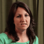 A person with shoulder-length dark hair in a green top stands by a green curtain, reflecting medbridge's fusion of digital healthcare and personal touch.
