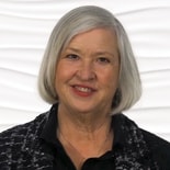 A smiling person with short gray hair in a black top is pictured on a white background for medbridge.