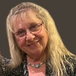 A woman with long blonde hair, glasses, and a necklace in a patterned top stands against a gray background for medbridge.