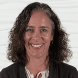 A smiling person with curly hair, wearing a dark jacket, embodies Medbridge's innovative digital healthcare approach.