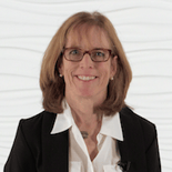 A smiling professional with glasses in a black blazer stands against a textured white background, symbolizing expertise in digital healthcare or medbridge-related software.