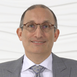 Man in a gray suit and glasses smiling against a white textured background for medbridge.