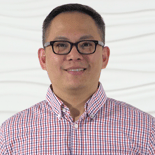 A person wearing glasses and a checkered shirt smiles against a textured wall, representing Medbridge's positive spirit in healthcare education.