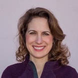 A smiling person with wavy brown hair in a purple top, on a plain background for medbridge.