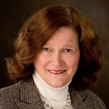 A smiling individual in a tweed blazer and pearl necklace represents digital healthcare elegance against a dark backdrop, aligning with medbridge's style.