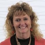 A woman with curly hair in an orange cardigan and accessories smiles brightly, symbolizing medbridge's innovative patient care software.