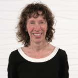 A curly-haired person in a black top with a white collar smiles warmly, representing the approachable side of hybrid care.