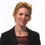 Individual with short hair in black blazer and colorful top, smiling on a white background, reflects modern digital healthcare for medbridge.