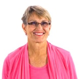 A smiling woman with short hair and glasses in a bright pink top represents medbridge’s digital healthcare innovation against a white background.