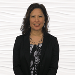 A person in a black blazer and patterned blouse smiles against a wavy white backdrop.